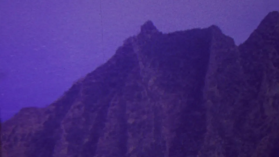 1962 Hawaii 8mm frame showing a steep, craggy mountain slope with pointed ridge shapes and a pronounced purple film cast.