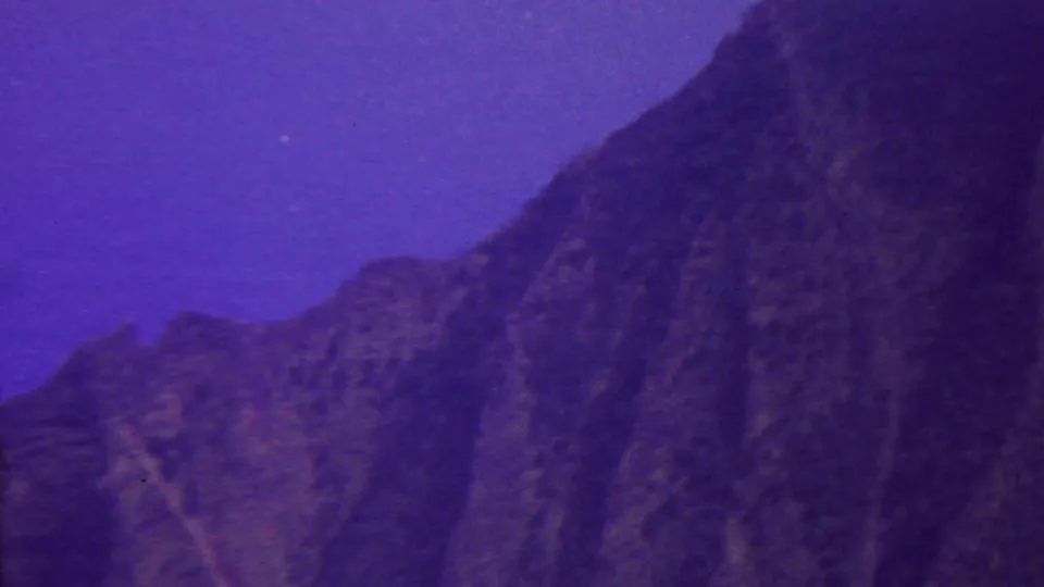 1962 Hawaii 8mm frame showing a dark mountain slope, lower ridgeline, and open purple-blue sky, with soft archival film texture.