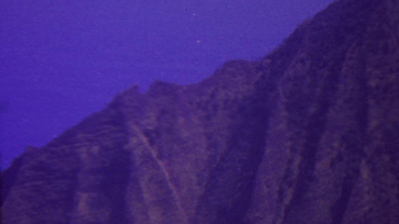1962 Hawaii 8mm frame showing a rugged mountain silhouette beneath a deep purple-blue twilight sky, with soft grain and low-light exposure.