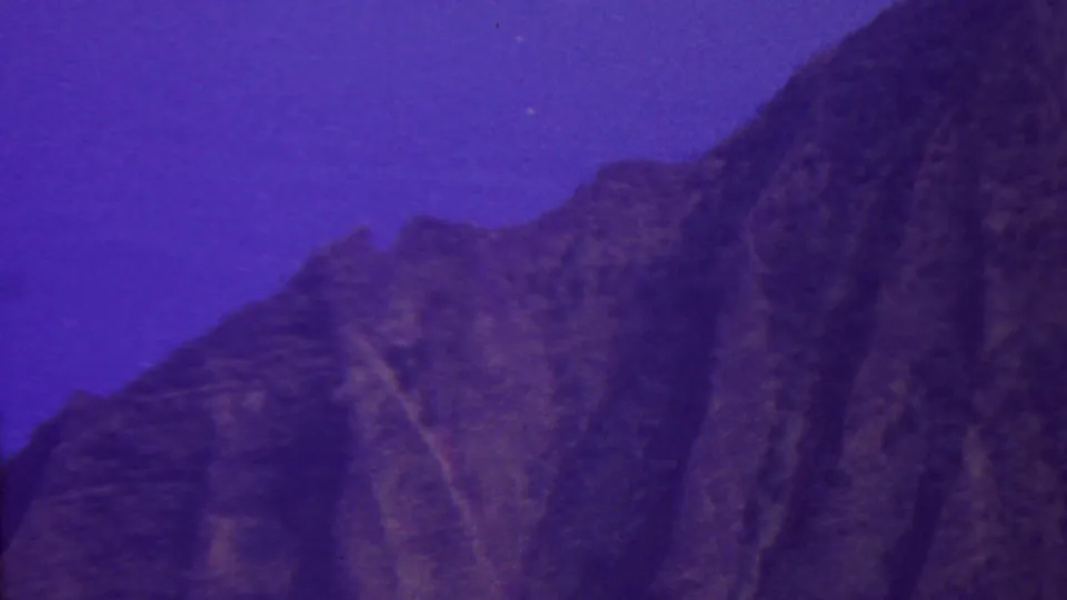 1962 Hawaii 8mm frame showing a rugged mountain silhouette beneath a deep purple-blue twilight sky, with soft grain and low-light exposure.