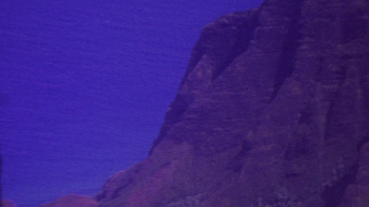 Close view of a steep rocky cliff with blue water behind it.
