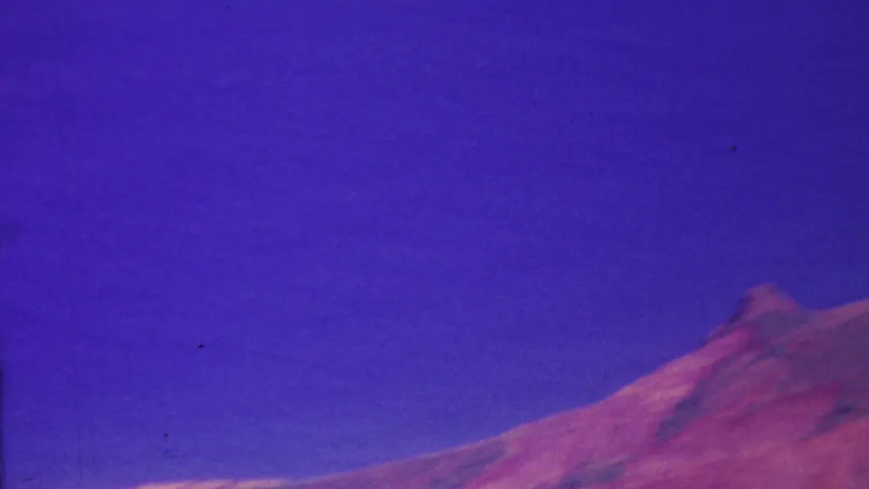 1962 Hawaii 8mm frame looking toward a reddish mountain shoulder and broad blue-purple sky, with the composition shifted lower and little water visible.