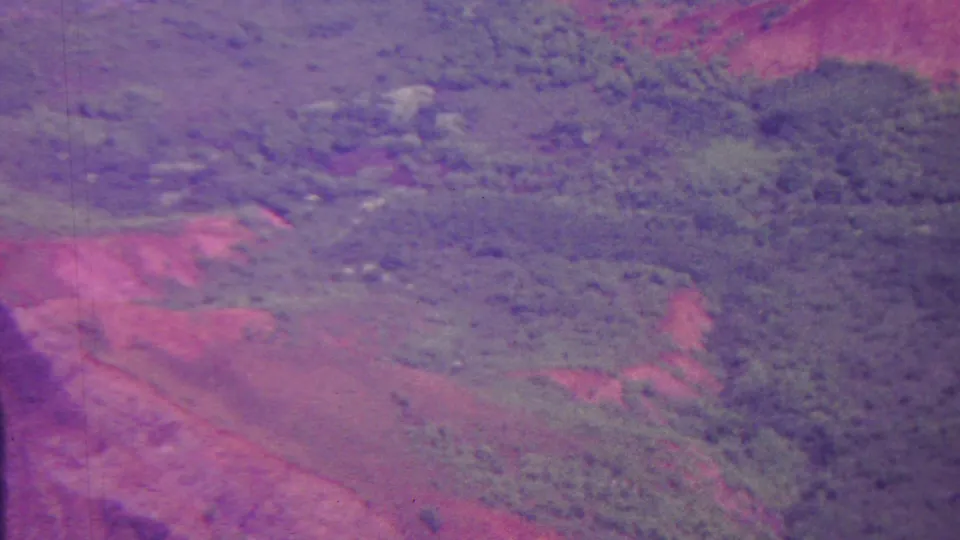 1962 Hawaii 8mm frame showing a broad valley-like landscape from above, with dense green growth, reddish earth, and soft aged-film texture.