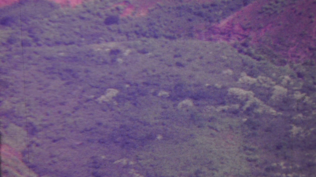 High aerial view of open mountainous terrain with brush and rocky outcrops.