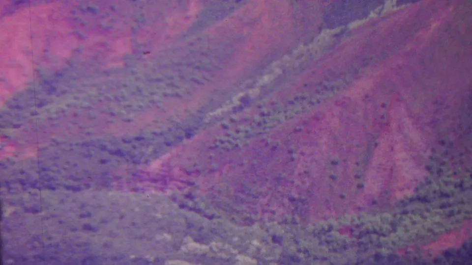 1962 Hawaii 8mm aerial frame with ridgelines, drainage-like gullies, sparse green vegetation, and pink-purple fading across the landscape.
