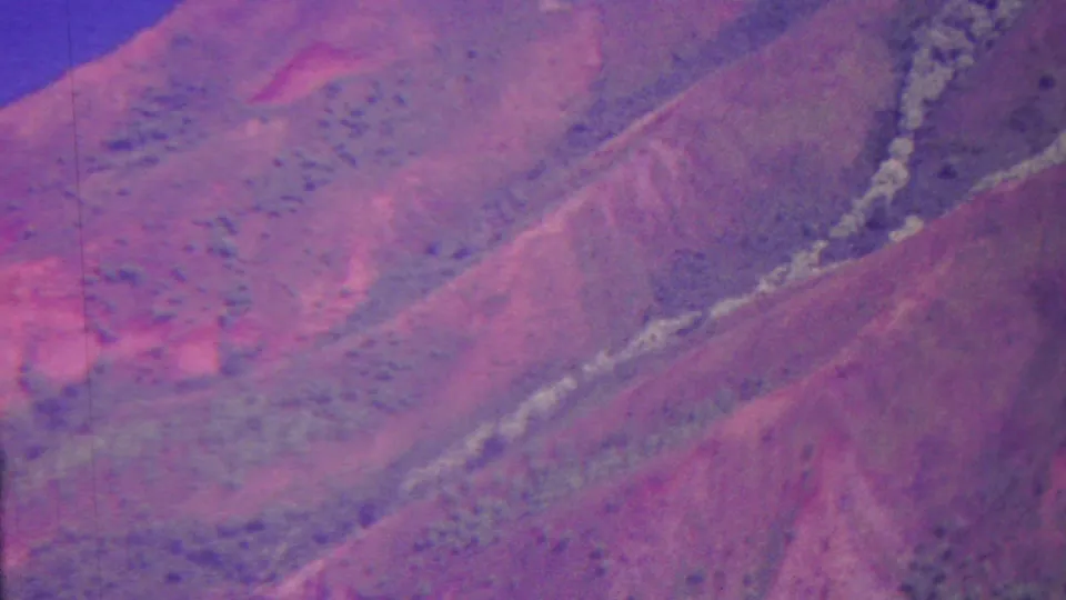 1962 Hawaii 8mm aerial view of steep mountainous slopes, a pale gully or drainage line, scattered brush, and strong magenta aging in the film image.