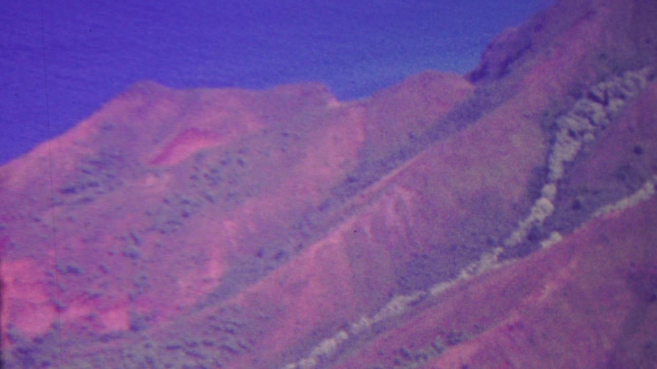 1962 Hawaii 8mm frame showing a steep, hazy mountain slope with muted vegetation and a blue-purple sky.