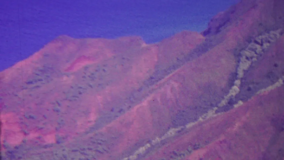 1962 Hawaii 8mm frame showing a steep, hazy mountain slope with muted vegetation and a blue-purple sky.