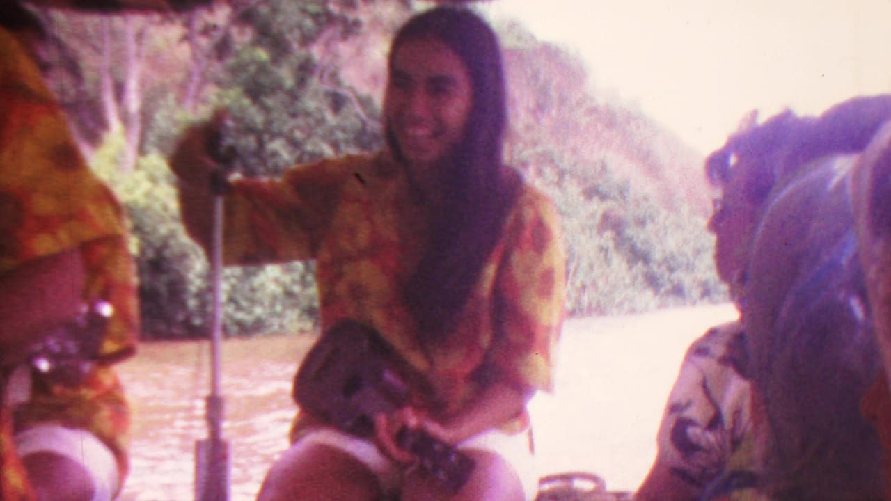 Woman in a floral shirt seated by a microphone with a ukulele on a boat.