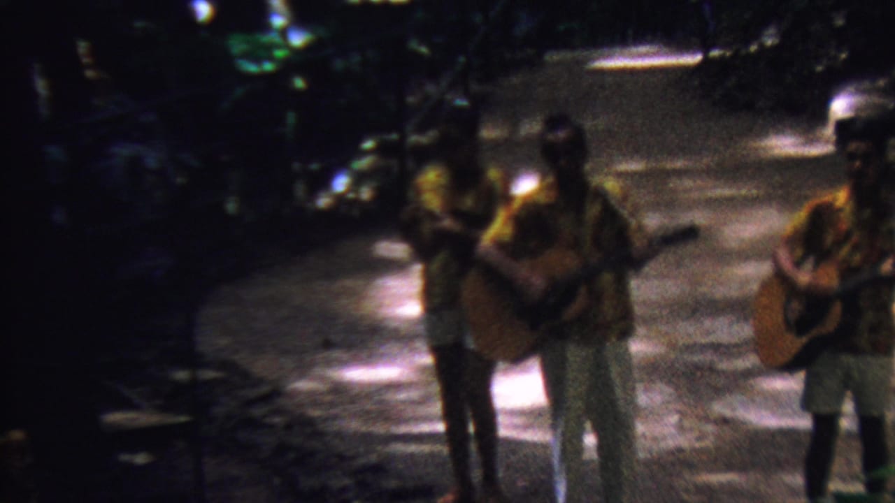 Three adult men in tropical shirts hold acoustic guitars on a shaded path in 1962 Hawaii home-movie footage.