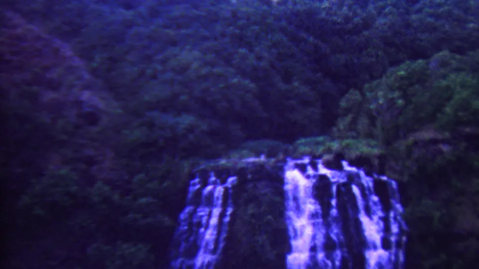 Water cascades over dark rock amid lush foliage in a 1962 Hawaii home-movie waterfall view.