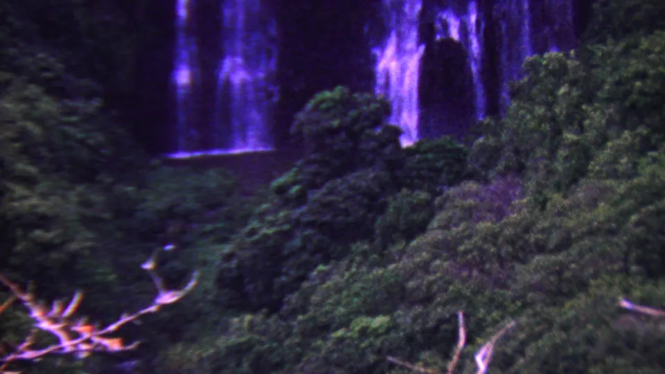 1962 Hawaii 8mm frame showing blue-purple waterfall streams dropping toward a small dark pool, partly obscured by dense tropical foliage.
