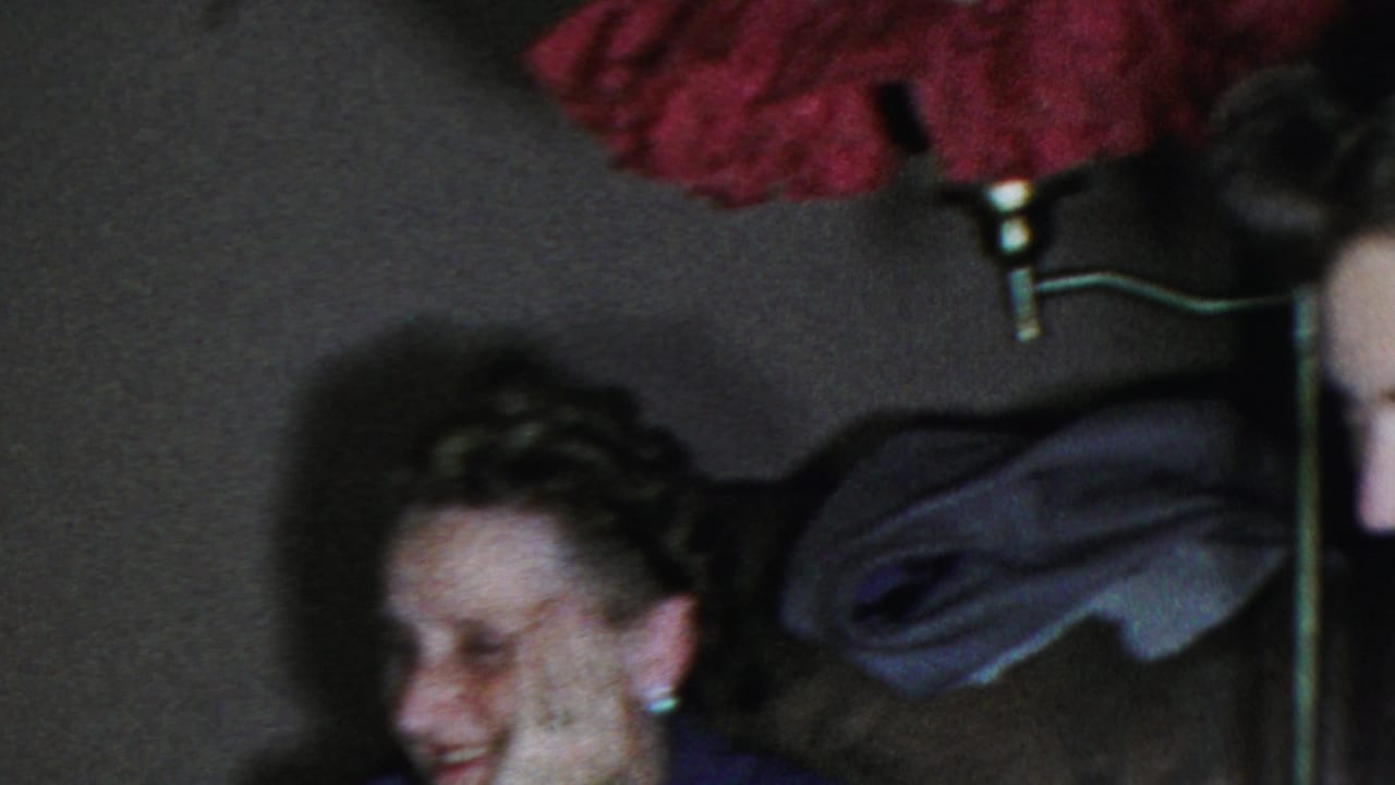 Adults appear to laugh together inside a private Columbus, Ohio interior, with a red patterned shade or fabric and dark household furnishings visible.