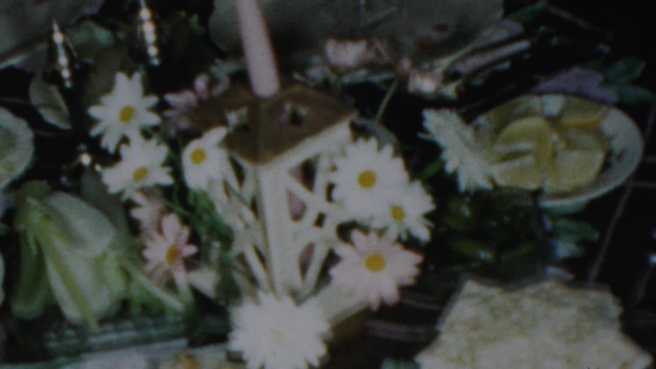 1954 Columbus, Ohio home-movie frame with white daisies around a candle lantern centerpiece, china plates, glassware, and arranged desserts on a formal table.