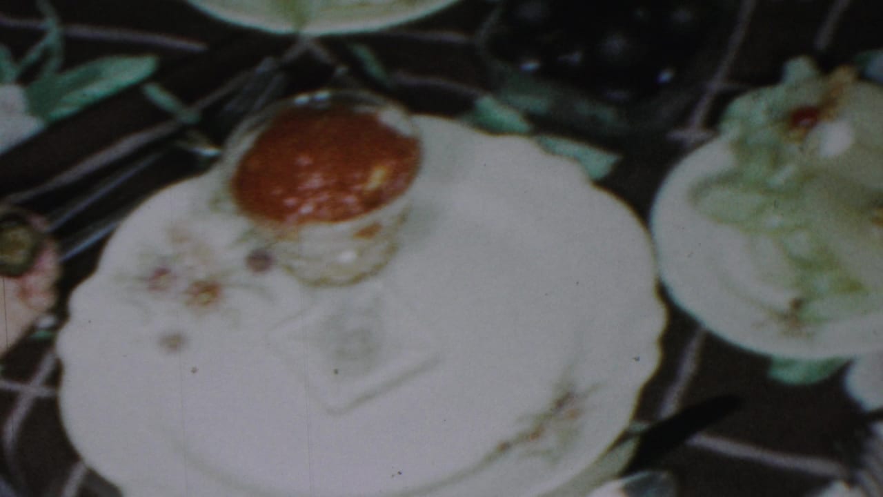 Close view of a floral plate and glass of red sauce on a dark tablecloth.