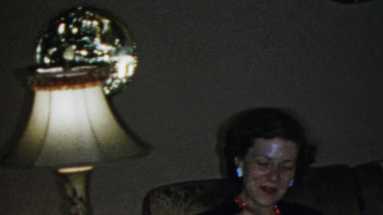Woman seated near a bright table lamp in a dark living room.