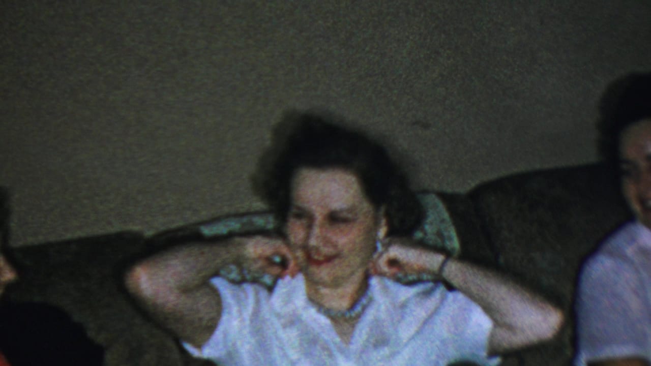 Woman seated on a couch smiling toward the camera in a dim room.