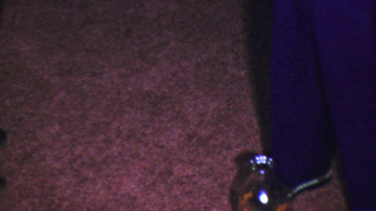 Tightly cropped home-movie frame from the supplied 1954 Columbus, Ohio clip showing the carpeted play area, partial children's legs, and a bottle used in the game.