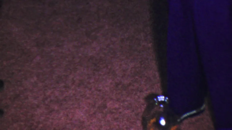 Tightly cropped home-movie frame from the supplied 1954 Columbus, Ohio clip showing the carpeted play area, partial children's legs, and a bottle used in the game.