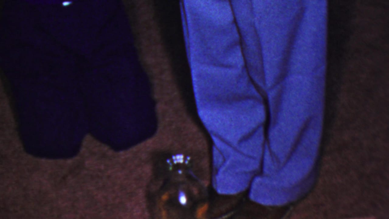Cropped legs in blue and dark pants stand beside a glass jar on carpet.