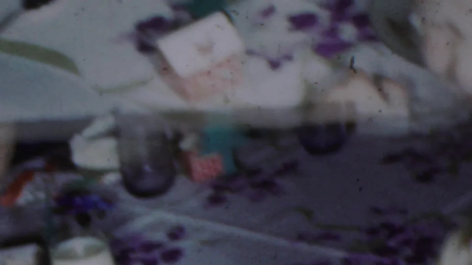 Blurred 8mm frame showing a pale patterned surface with purple and green markings, with no identifiable people, logos, or location details visible.