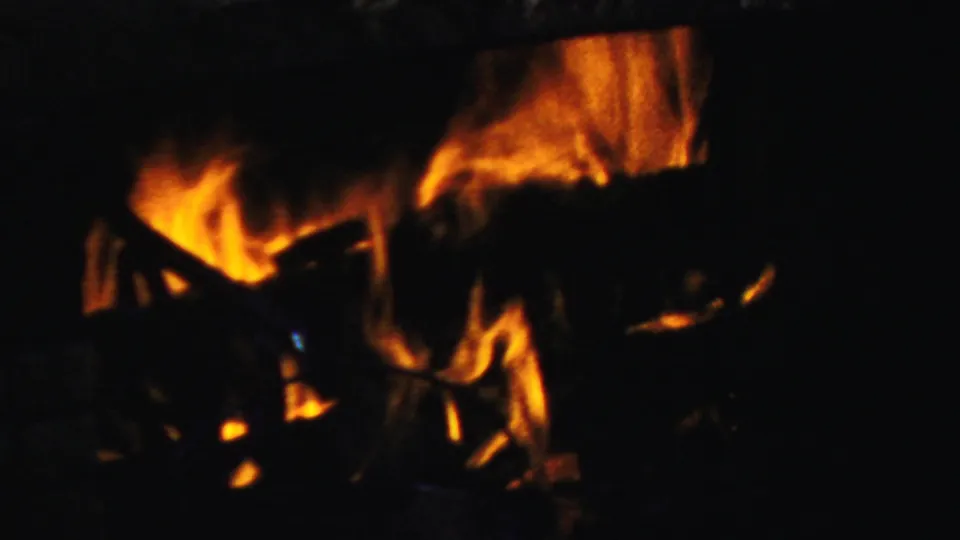 1954 Columbus home-movie frame of orange flames rising around dark wood logs in a shadowed fireplace, with heavy grain and warm exposure.