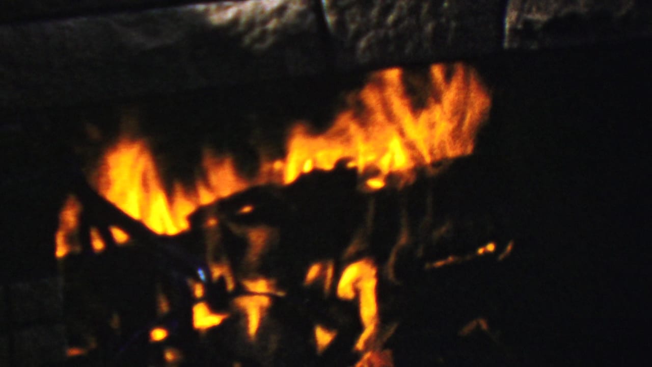 1954 Columbus, Ohio 8mm frame showing orange flames and charred logs within a dark stone fireplace opening.