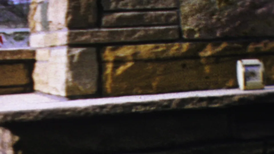 Final 8mm frame of the Columbus fireplace showing the masonry surround, mantel ledge, and small clock in a mid-century interior.