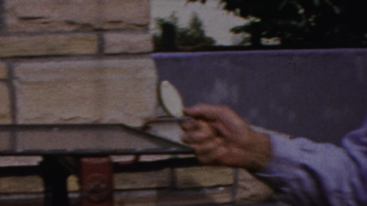 Hand holding a metal grill wheel or handle near a stone wall.