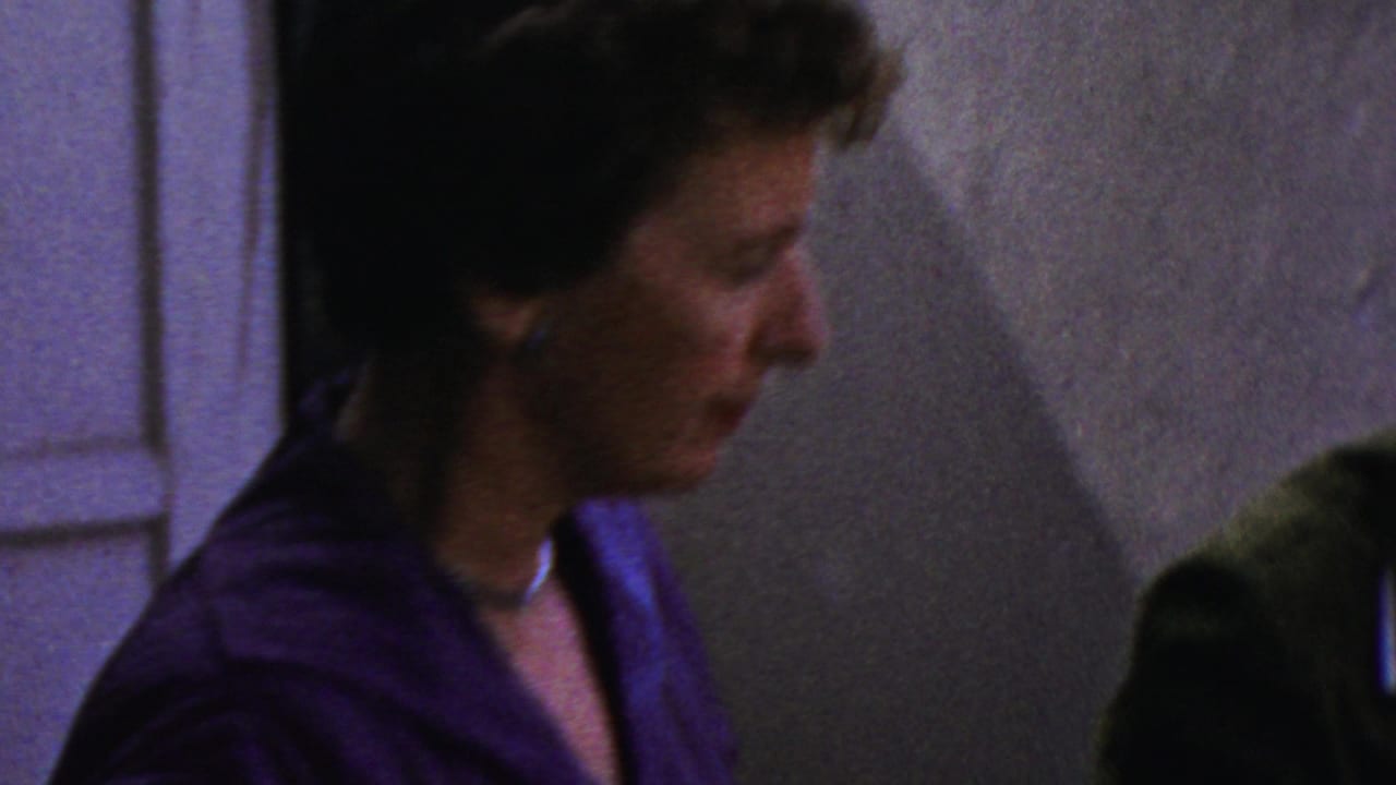 In Columbus, Ohio home-movie footage from 1954, a woman in a blue dress and choker is seen in profile near an indoor buffet table.
