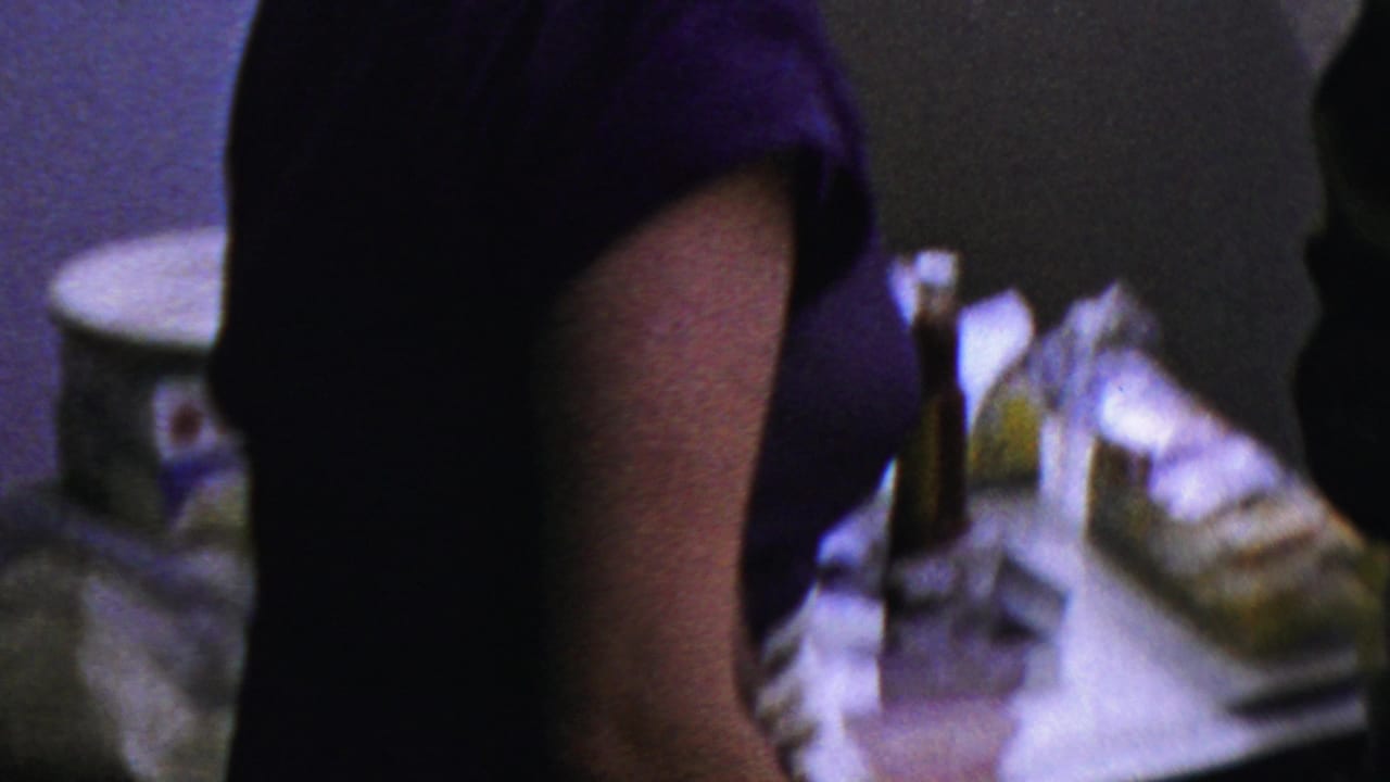 A guest in a dark blue or purple dress stands close to a buffet table with plates and food during the 1954 Columbus indoor gathering.