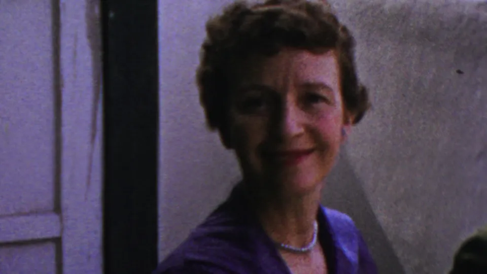 The woman in the blue dress smiles toward the camera inside a private Columbus, Ohio interior, with a door and wall visible behind her.