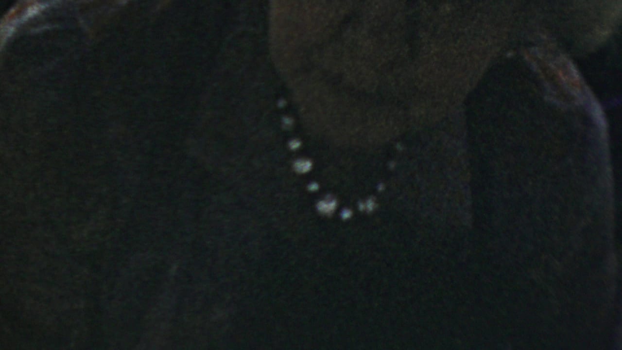 Close side view of an older woman with glasses and a pearl necklace.