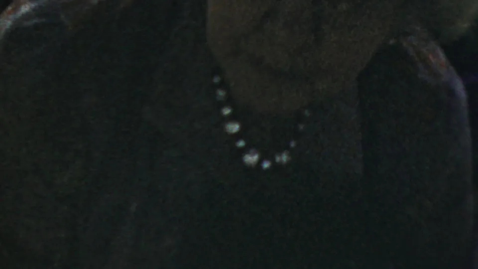 Close side view of an older woman in glasses and pearls, softly focused in low-light 1954 Columbus, Ohio home-movie footage.