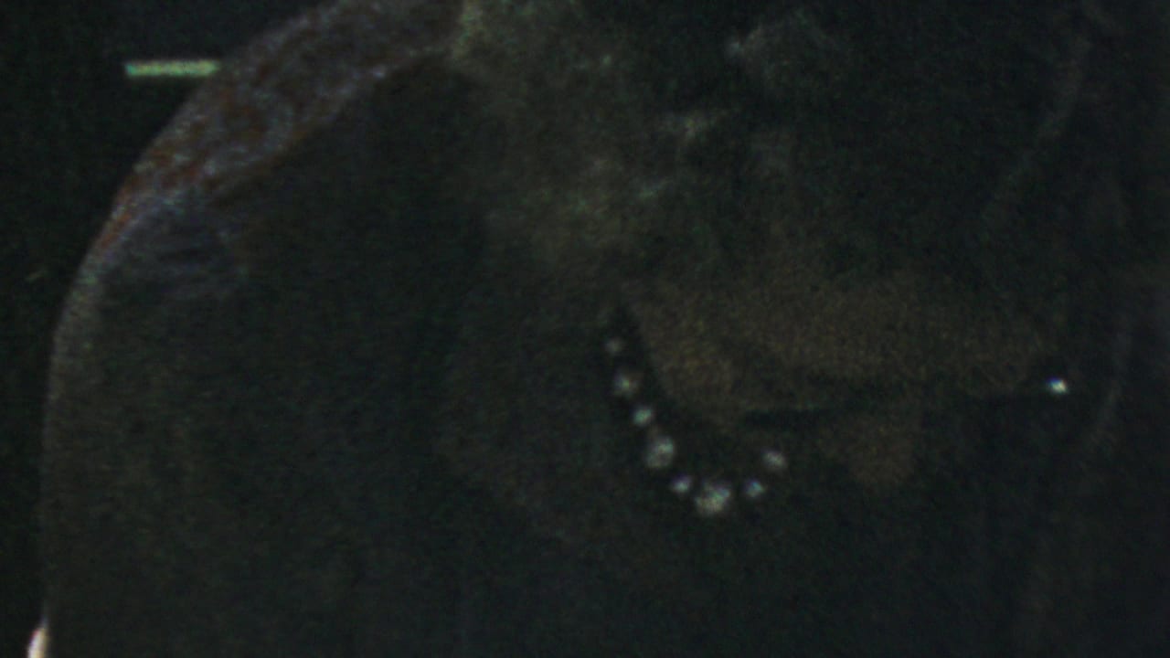 Close 1954 Columbus home-movie frame of a woman in a dark dress and pearl necklace at a dim family dinner table.