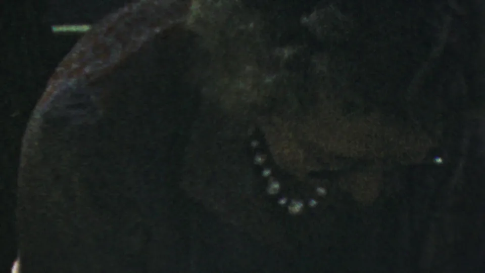 Close 1954 Columbus home-movie frame of a woman in a dark dress and pearl necklace at a dim family dinner table.