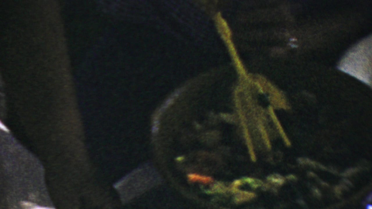 Serving tongs held over a bowl of mixed vegetables or salad in low light.