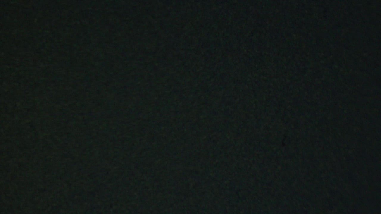A low-light restaurant frame shows a man in a dark suit partially obscured by a wooden chair back, with the surrounding interior rendered in dark greenish 8mm tones.