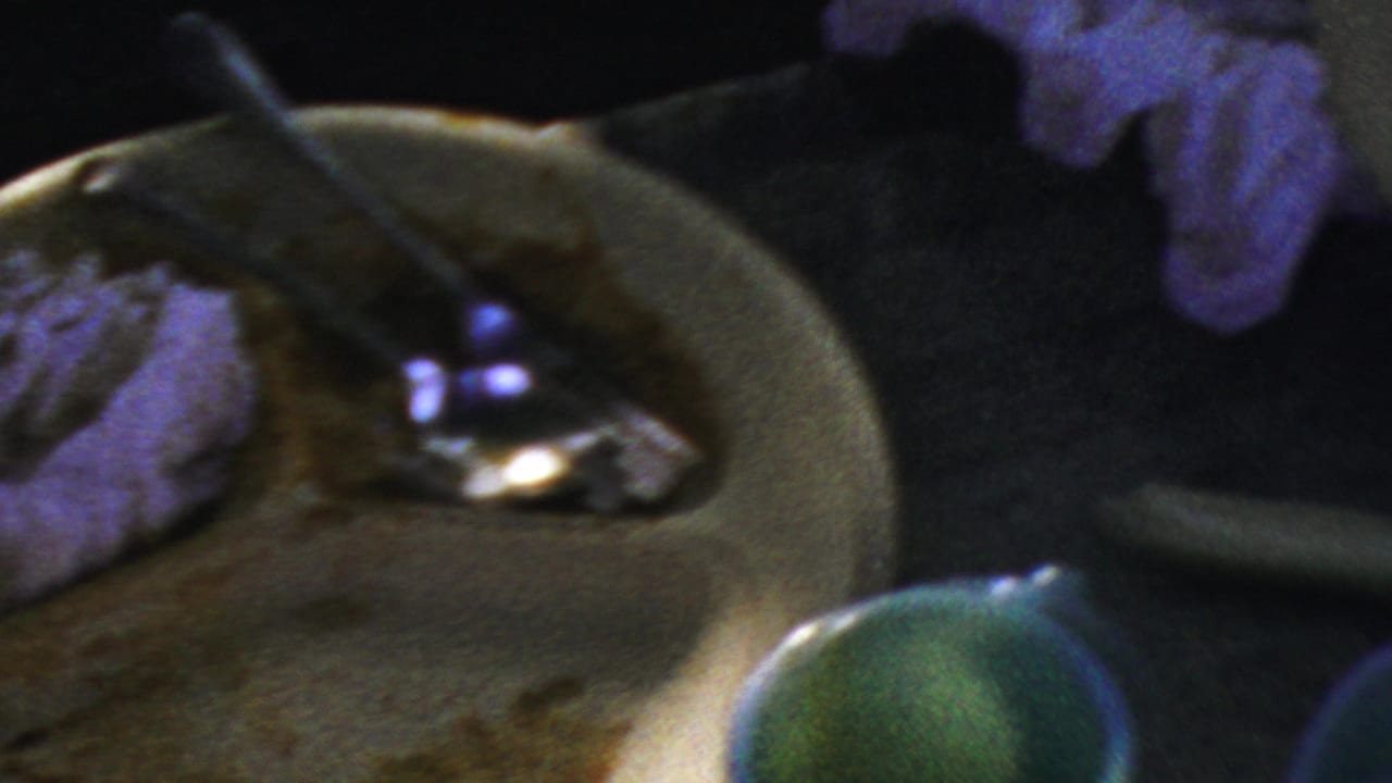 Close view from 1954 Columbus home-movie footage showing dirty plates, leftover food, a spoon, and dim blue-tinted table lighting after a party.