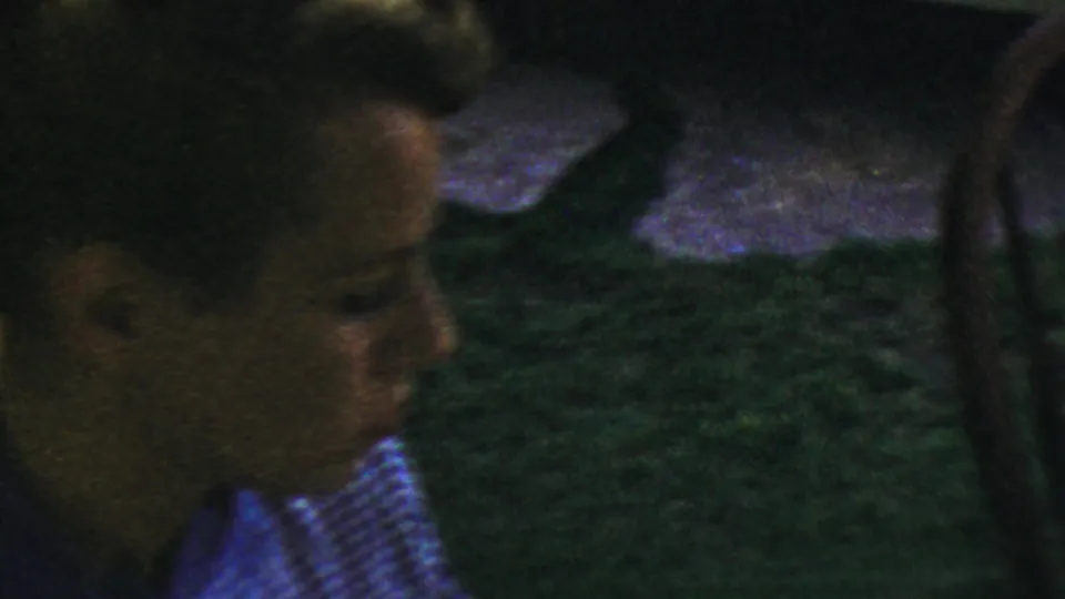 A partially visible person in a checkered shirt appears near wooden dining chairs in this 1954 Columbus, Ohio home-movie interior.