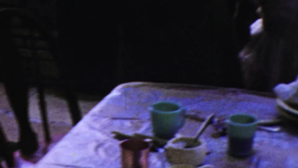 A dining table with green cups, bowls, utensils, and a cloth is seen in the 1954 Columbus, Ohio home-movie scene.