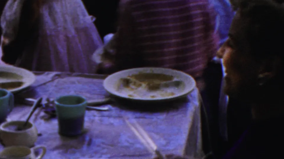 1954 Columbus, Ohio 8mm frame showing a family gathering from above the dinner table, with used plates, colored cups, utensils, and people passing through the room.