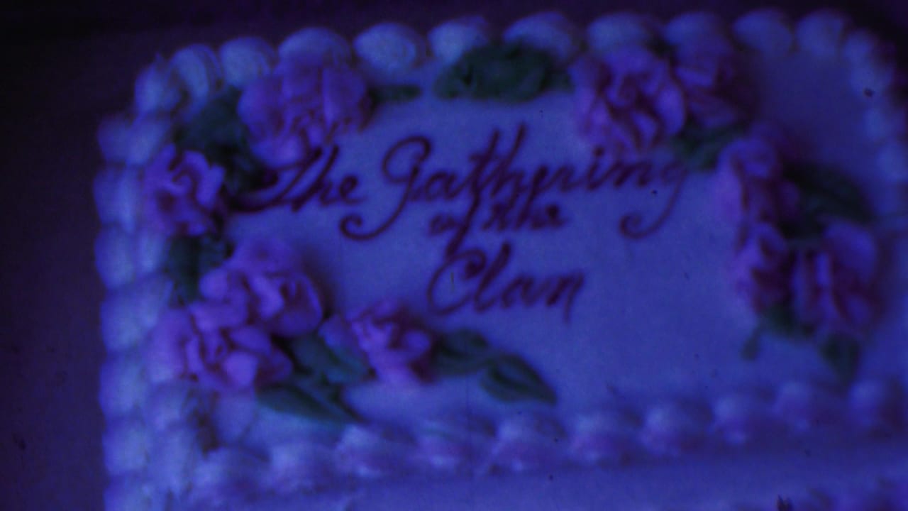 1954 Columbus, Ohio 8mm frame showing a soft-focus decorated celebration cake with purple floral icing and the words The Gathering of the Clan under a strong blue color cast.