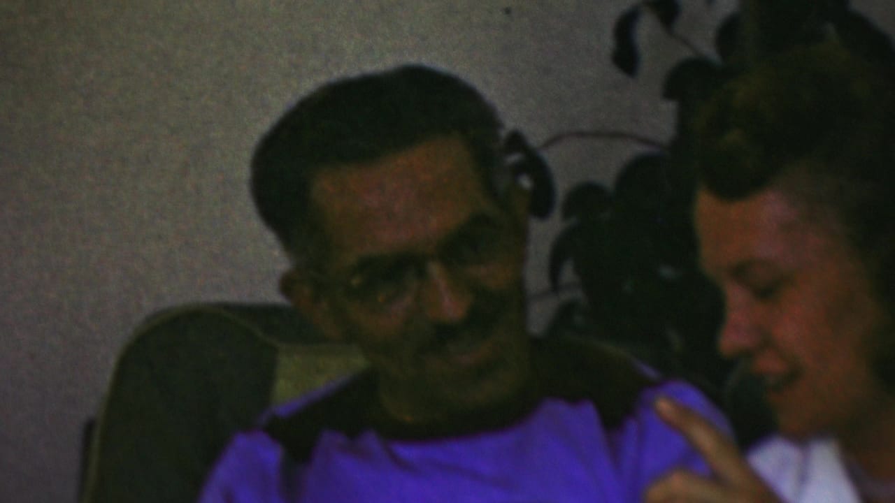 Man seated on a couch beside a woman in conversation.