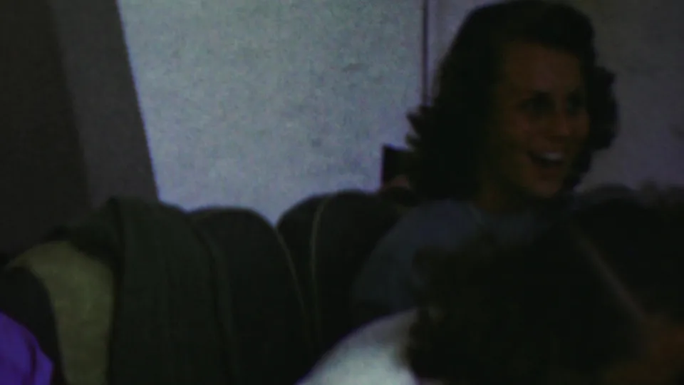 Several adults sit close together in a private living room, with one woman smiling and another figure turned in profile during the 1949 Seaside, New Jersey home-movie scene.