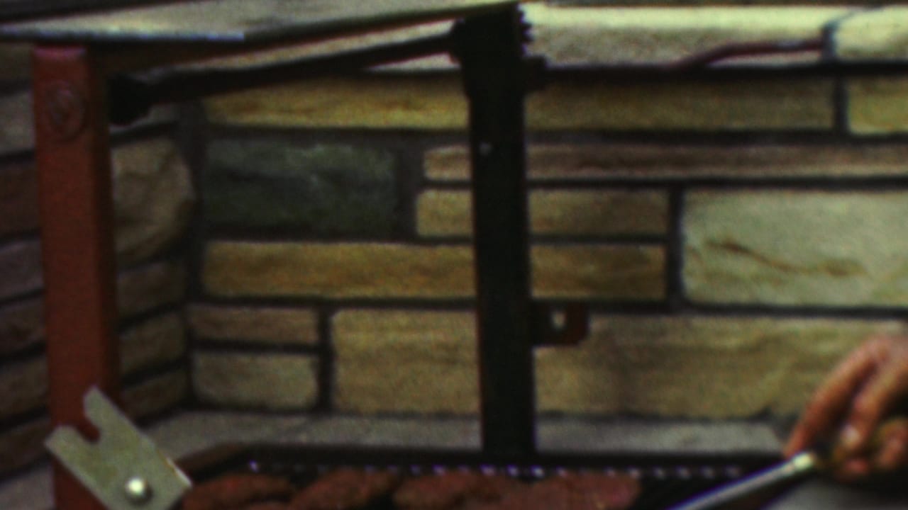 A 1949 Seaside, New Jersey home-movie frame shows the stone backdrop and metal supports of an outdoor grill with coals visible along the lower edge.
