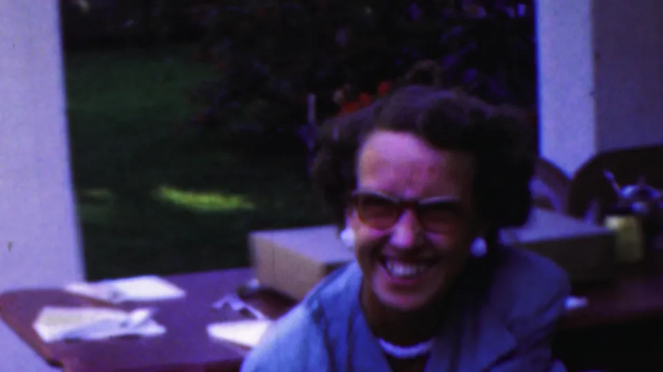 A woman with dark curly hair and glasses laughs at an outdoor table in Seaside, New Jersey, in footage identified as 1949 8mm home movie material.