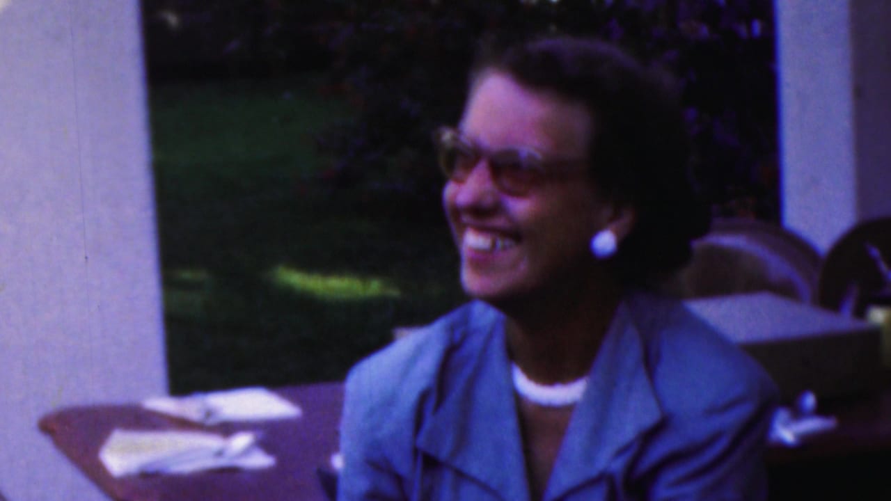 Woman in a blue jacket and glasses smiling at an outdoor table.