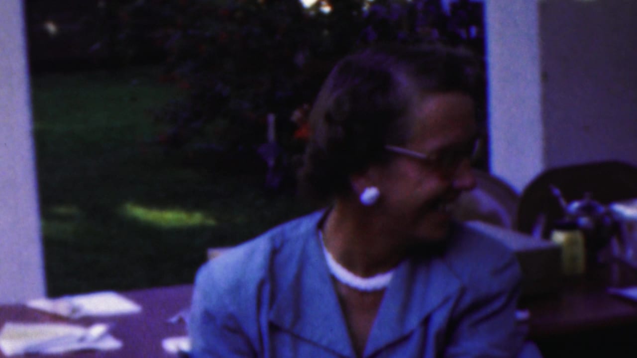 Woman in glasses turns to the side while seated at an outdoor table.