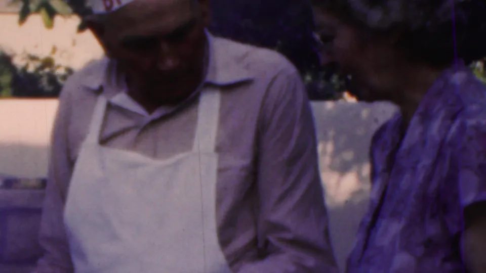 A 1949 Seaside, New Jersey home-movie frame shows the apron-wearing man looking down at the cookout area as the woman stands beside him.